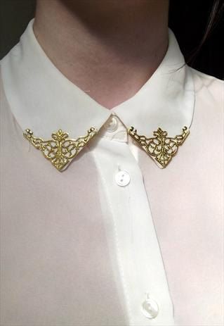 loseup view of a woman wearing a white collared shirt adorned with a gold, ornate, lacelike collar accessory. the accessory is positioned on the shirt's collar, adding a decorative and elegant touch to the simple shirt. the image focuses on the detail of the jewelry and its placement on the collar. the overall style is feminine and sophisticated.