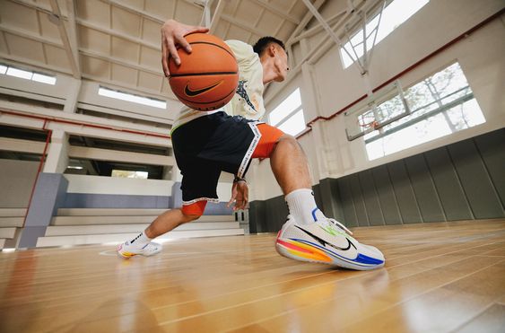 a basketball player in nike athletic wear dribbles a basketball on an indoor court. the image is taken from a low angle, highlighting the player's dynamic movement and stylish sportswear.