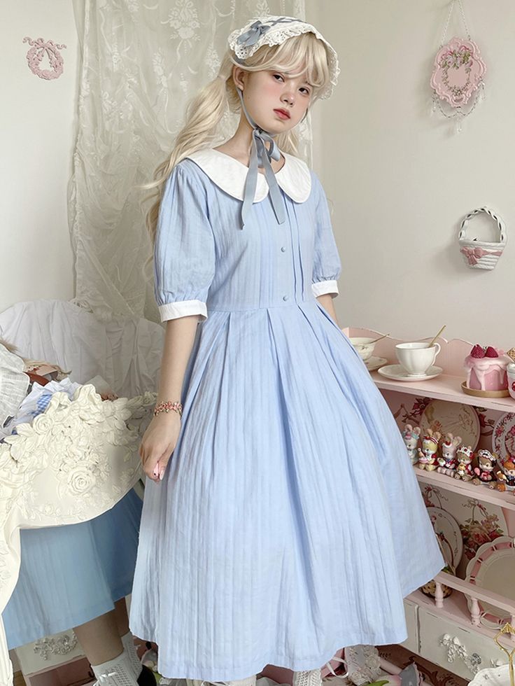 a young woman poses in a blue lolitastyle dress with white collar and cuffs. she is also wearing a white lace headband. the background is a bedroom with a vintage feel. the image has a soft, dreamy quality.