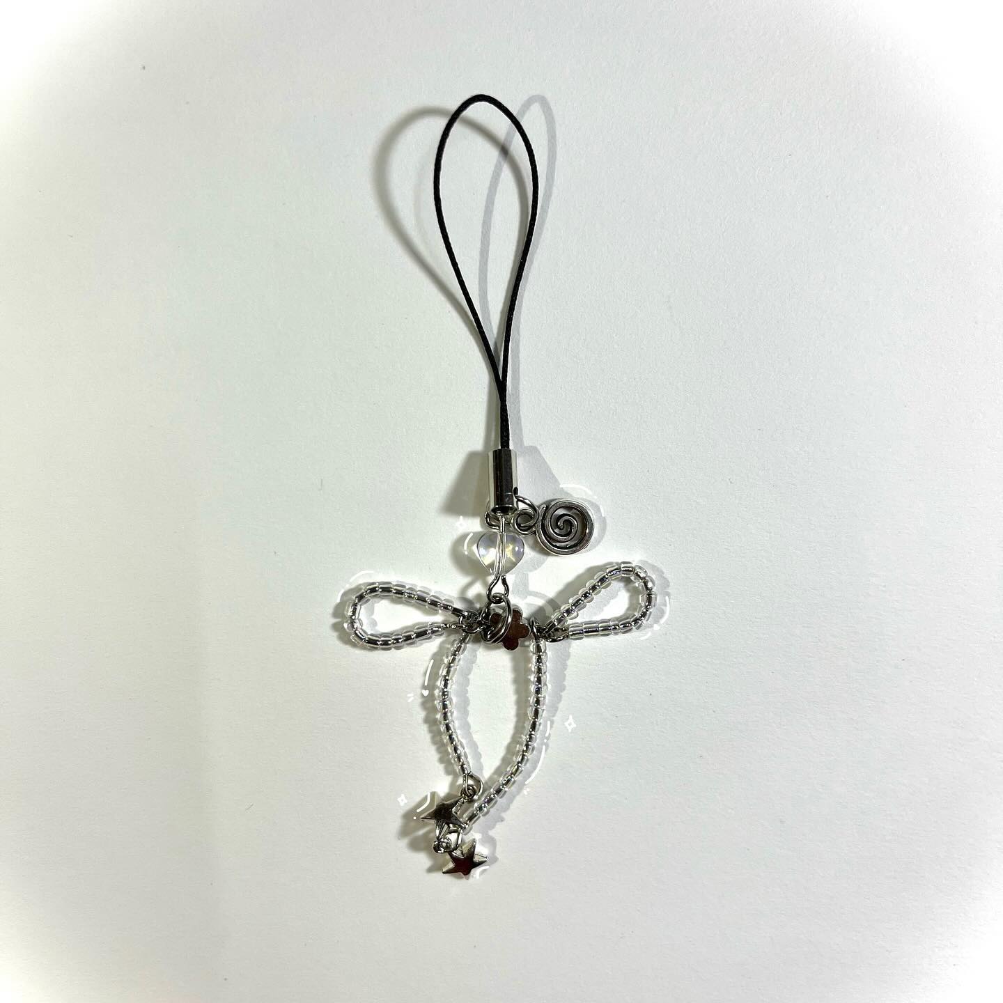 a closeup shot of a handcrafted silver keychain with a decorative design. it consists of a loop for attachment, a spiral wire design, clear beads, a beaded angellike shape, and two small star charms hanging at the bottom. the keychain is isolated against a white background.