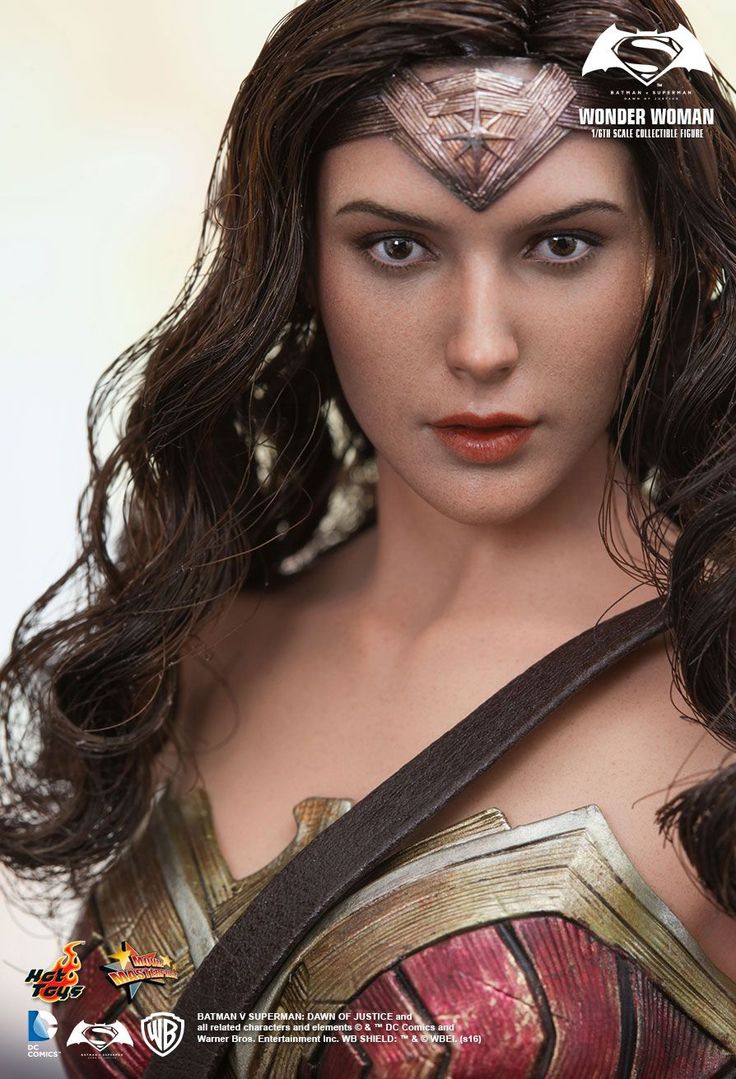 a closeup image of wonder woman's face from the hot toys 1/6 scale collectible figure. wonder woman is wearing her iconic golden armor and a leather strap across her chest. the image is taken from a slightly upward angle and highlights her delicate features, sharp cheekbones, and piercing gaze. the background is a soft, outoffocus blur, giving the image a more intimate and focused feel.