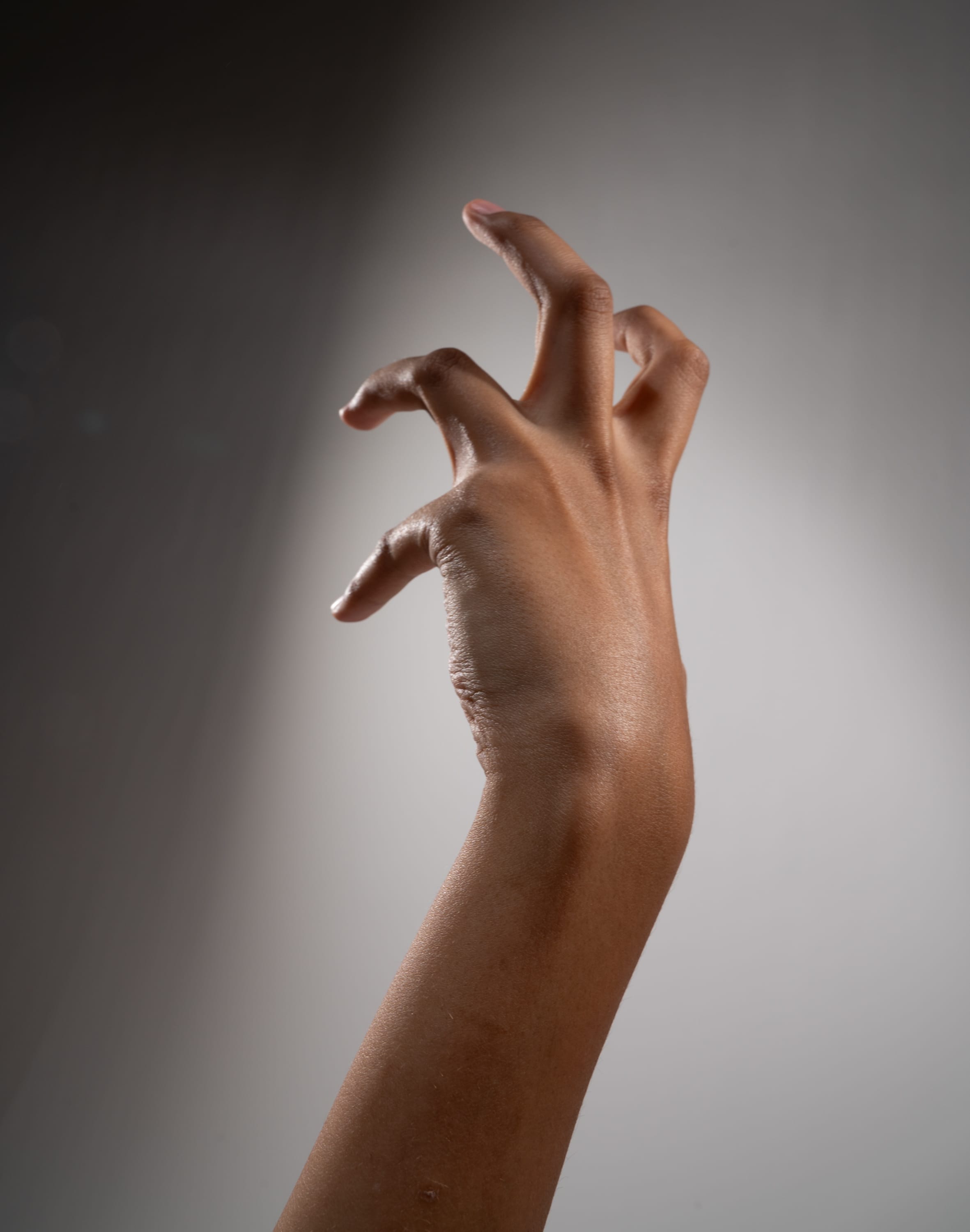 a closeup image of a hand with dark skin tone against a gray background. the hand is in a clawlike gesture, with fingers curled inward. the lighting highlights the texture and details of the skin.