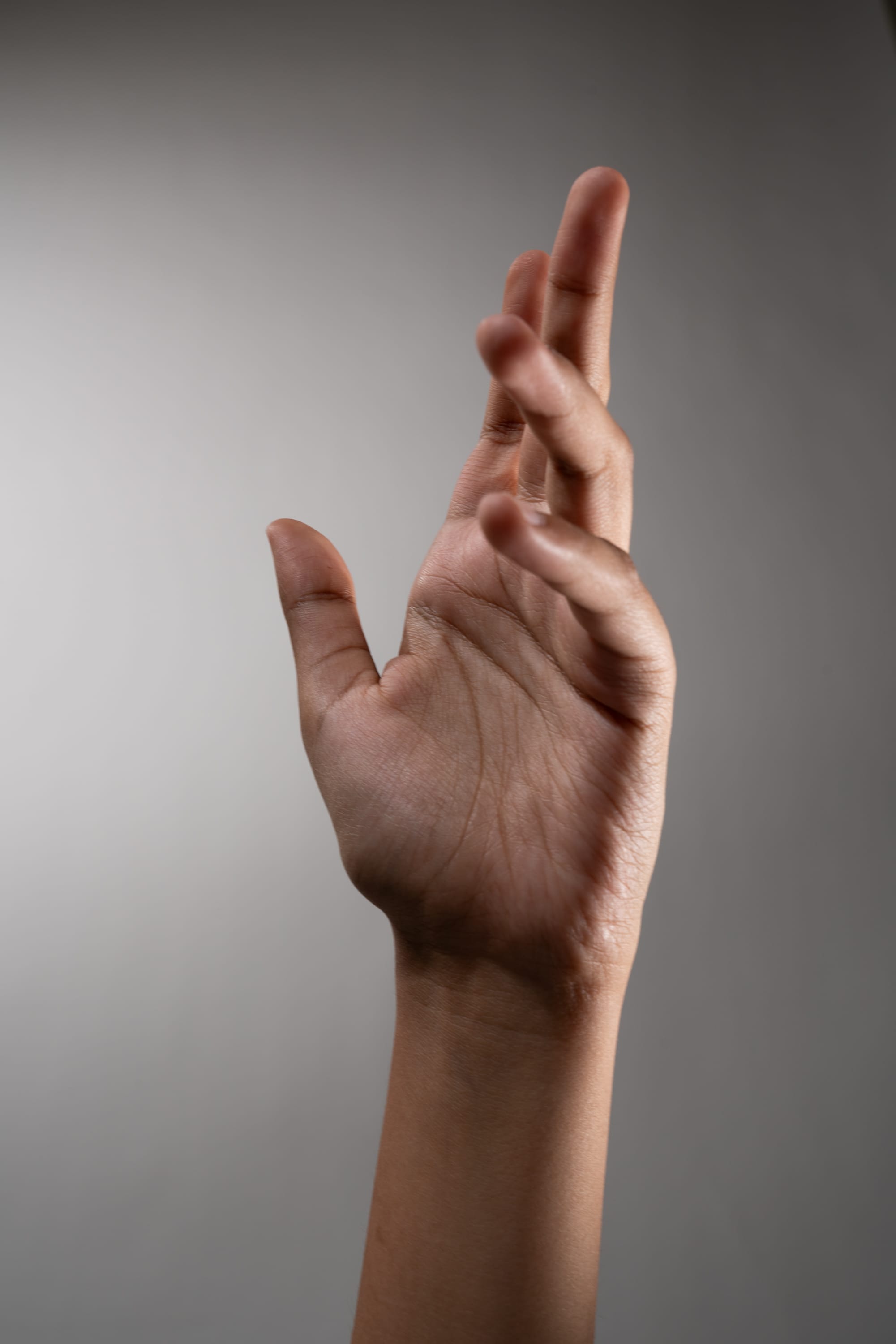 a closeup image of a hand and arm extended upwards against a gray background. the image is welllit with studio lighting, showcasing the details of the hand and arm.