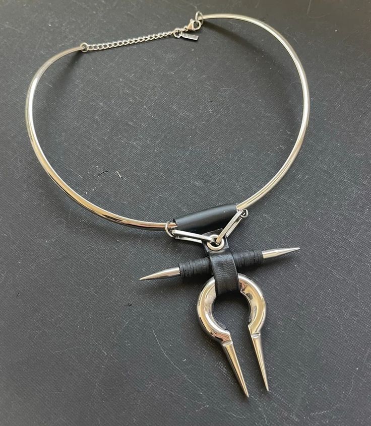 this is a close up of a silver choker necklace with a unique pendant. the pendant is made of metal and leather, and it has a sharp, pointed design. the choker is simple and elegant, and the pendant adds a touch of edgy style.