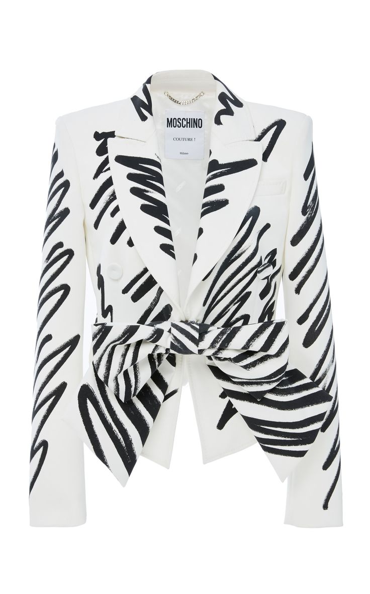 a white blazer with black brushstrokelike markings all over the front and sleeves. the blazer has a doublebreasted closure with a tie around the waist. the inside lining can be seen with the moschino label visible. the blazer has a structured silhouette with pointed shoulders.