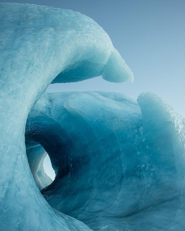 a closeup shot of an ice cave, formed by a glacier. the ice is a beautiful blue color, and the cave is lit by the sunlight. the ice cave looks like a tunnel leading somewhere unknown.