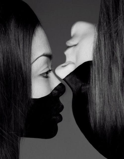 this black and white photograph captures two women, their faces partially hidden by a mysterious black makeup. the image is a study in contrasts and shadows, with the women's features emerging from the darkness. their gaze, their lips, and their close proximity create a sense of intensity and mystery, leaving the viewer to interpret their relationship and the emotions at play. the photograph is a captivating and provocative portrait, a timeless and elegant work of art.