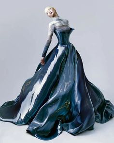 a fashion model poses in a stunning blue metallic gown. the dress is formfitting and features a dramatic, flowing skirt. the model's hair is styled in a simple, sleek look, and her makeup is minimal. the image is set against a white background, and the lighting is soft and diffused. this photo captures the elegance and sophistication of high fashion.