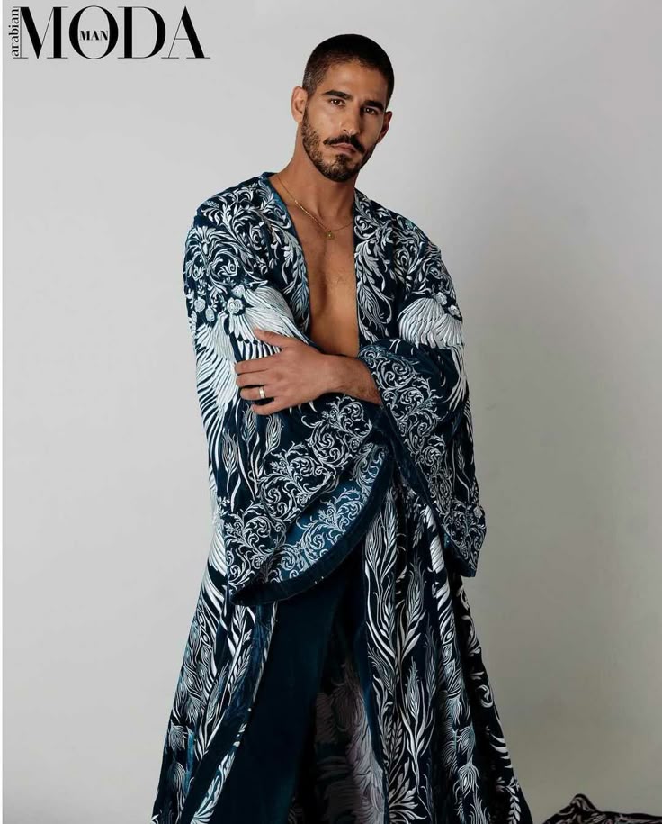 a male model is posing for a fashion magazine. he is wearing a long, patterned velvet robe and a gold chain. he has a beard and mustache. the magazine's logo, "moda man arabian," is in the upper left corner.