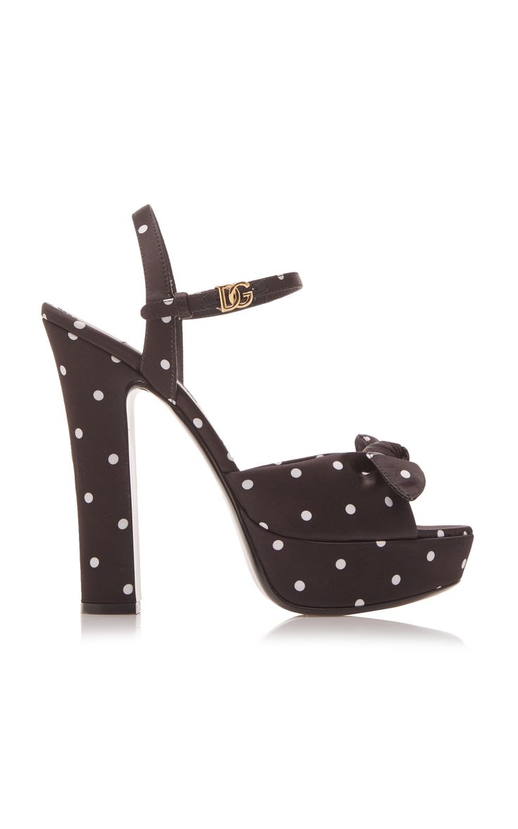 a studio shot of a single dolce & gabbana women's platform sandal. the shoe is black with white polka dots, has an ankle strap with a gold logo, and a platform sole. the style is elegant and dressy, suitable for summer or special occasions.  the shoe is shown from a side profile, showcasing its details and design features.
