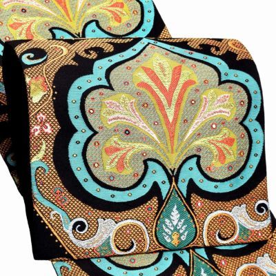 the image shows a closeup of a patterned textile with a paisley design. the fabric features a mix of colors, including black, gold, turquoise, orange, and green, arranged in intricate ornamental motifs. the dominant pattern is a stylized paisley shape, repeated across the fabric. the design gives off a traditional or vintage vibe.