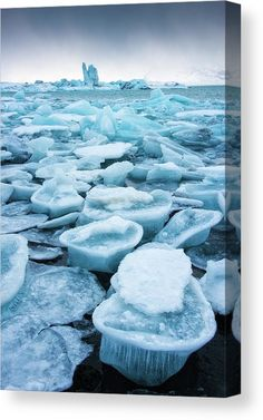 this image shows a landscape filled with various sized chunks of blue ice on what appears to be a shore. in the background, larger icebergs can be seen amidst the flat body of water and a cloudy sky. the scene suggests a cold, wintery environment with icy formations scattered across the foreground and extending into the horizon.