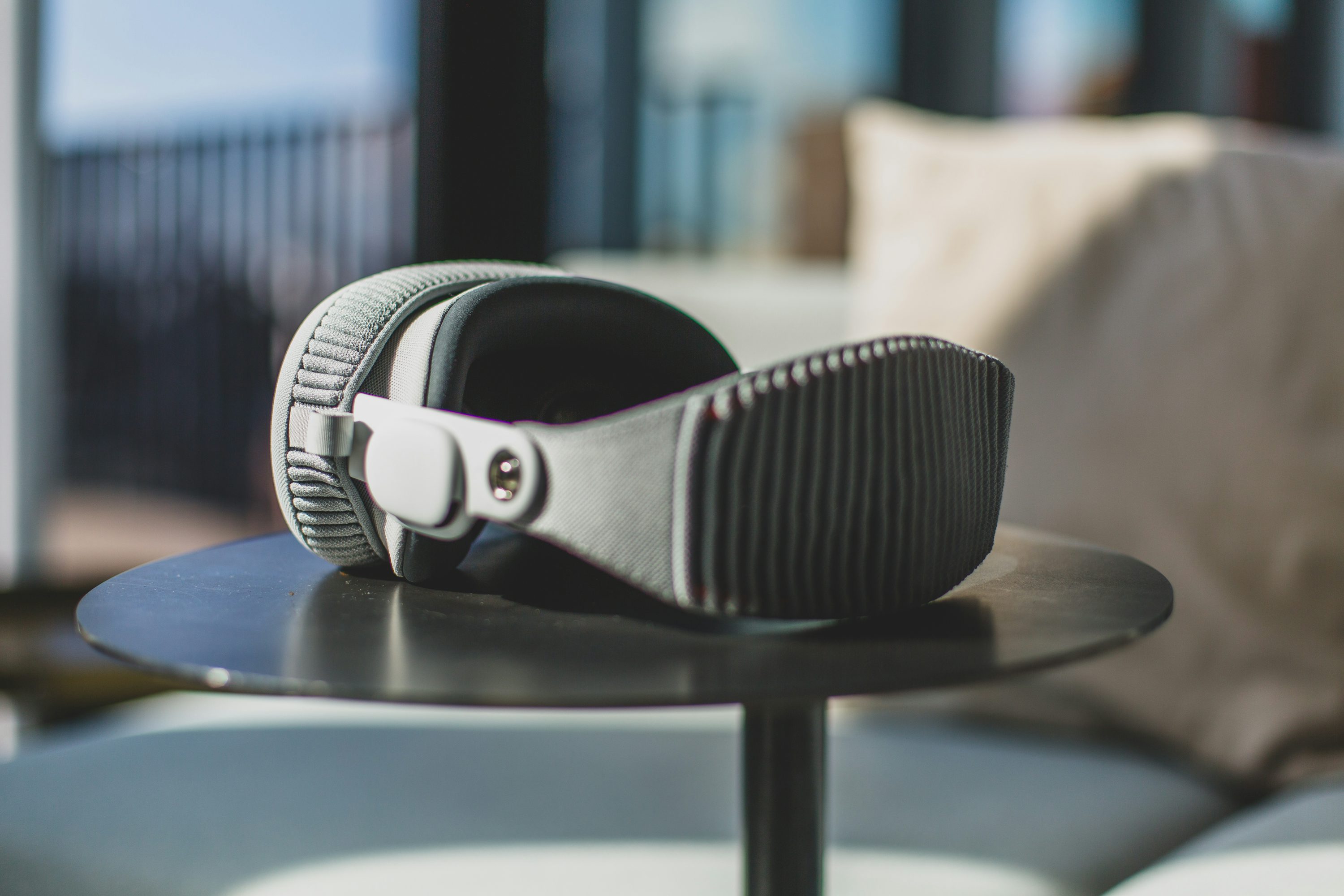 a pair of grey headphones sitting on a small black table, with a pillow and other furniture in the background.