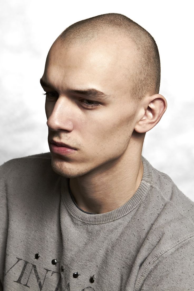 closeup portrait of a young, attractive man with a shaved head. he's wearing a grey sweatshirt and has a serious, contemplative expression on his face. the background is a plain white.  the image is welllit and professionally taken, possibly for a fashion or modeling portfolio.