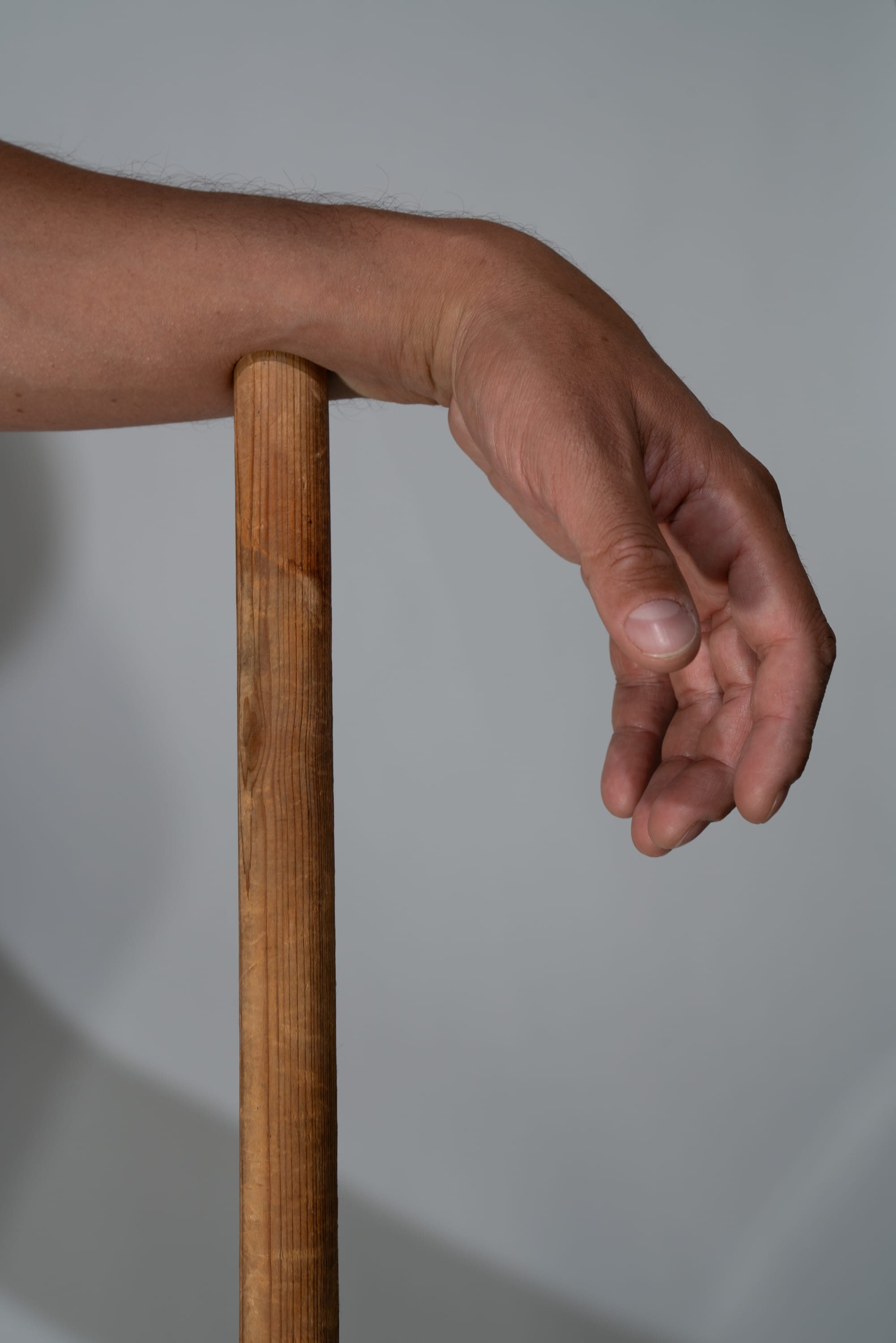a closeup view of a fairskinned male arm and hand resting on a vertical wooden stick.  the photo is taken in natural light indoors.