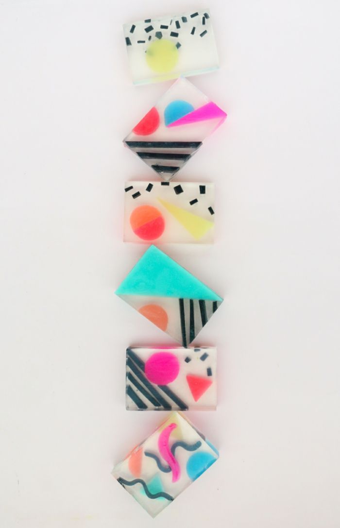 a set of six colorful geometric soap bars, arranged vertically on a white background. the soap bars feature abstract designs, with shapes, colors, and patterns. each soap bar has a different design, but all of them have a modern, minimalist aesthetic. the soap bars are perfect for a gift or for adding a pop of color to your bathroom.