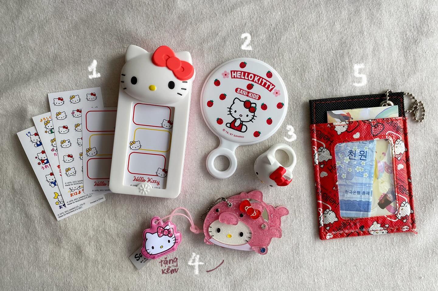 the image shows a collection of hello kitty items, including stickers, a mirror, a ring, two keychains, a wallet, and a name tag holder. all the items are in a white or lightcolored background.