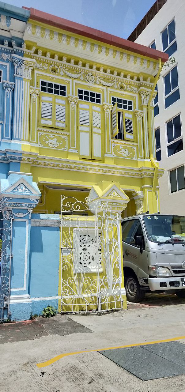 a yellow shophouse in singapore with ornate details and a wrought iron gate in front of it. the shophouse is a common type of building in southeast asia, dating back to the colonial era. the shophouse is characterized by its narrow facade, with a row of windows on the upper floor. the shophouse is typically made of wood or brick, and is often painted in bright colors.
