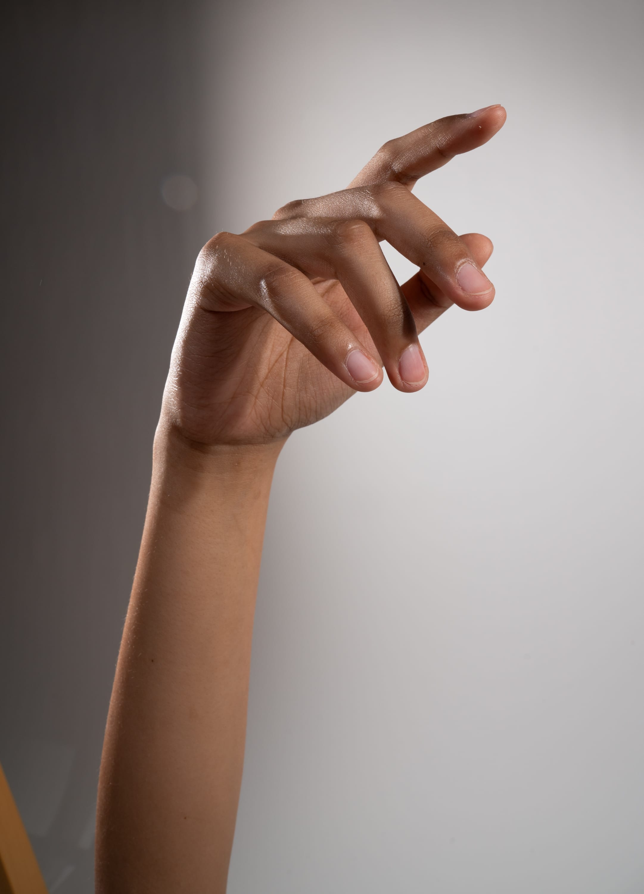 a closeup image of a woman's hand and arm, illuminated by studio lighting. the hand is extended towards the camera in a gesture, with the fingers slightly curled. the skin is smooth and has a warm undertone. the background is a neutral gray.