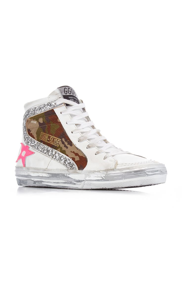a closeup shot of a golden goose slide hightop sneaker. the shoe is predominantly white leather with a camouflage pattern detail on the side and glitter accents.  a pink star is visible on the side. the shoe is presented on a white background.