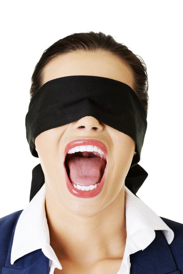 a woman wearing a black blindfold screams with her mouth wide open. she is wearing a white collared shirt and a dark blue jacket. she is looking scared and surprised.