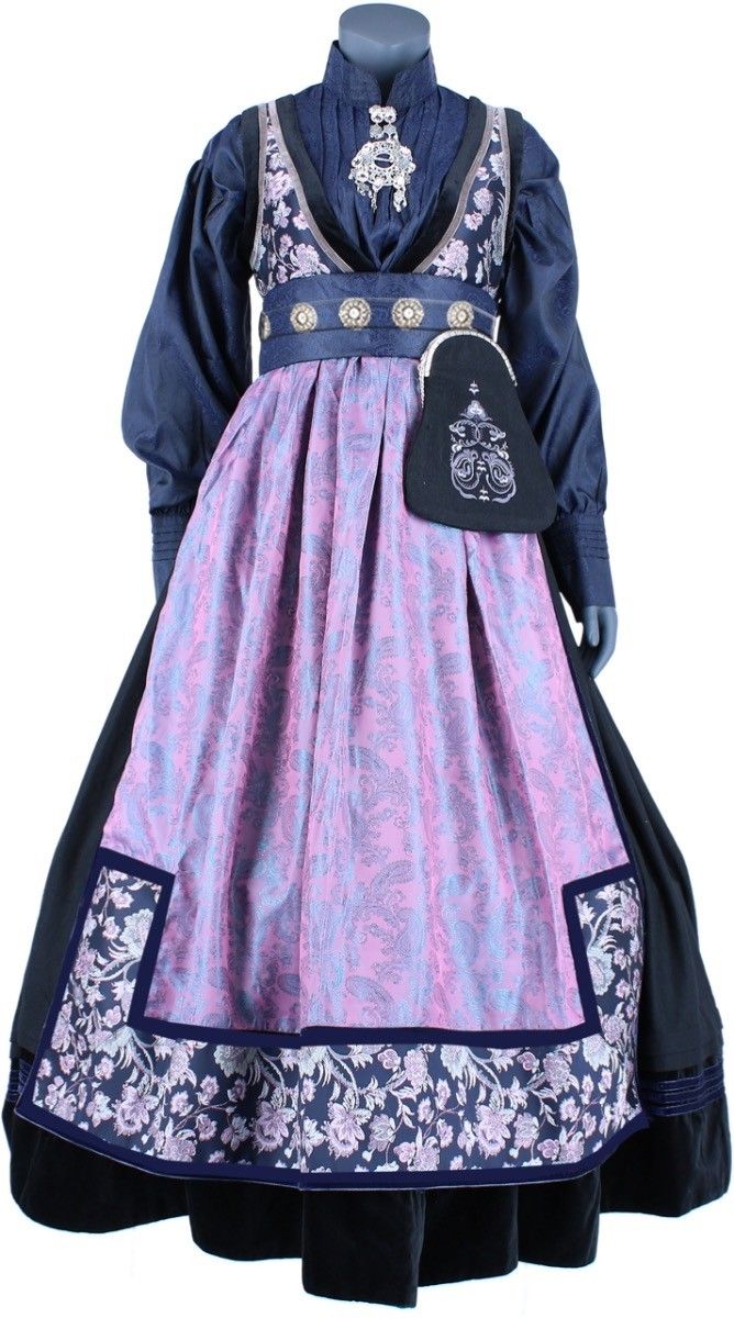 a fulllength studio shot features a mannequin dressed in a traditional norwegian bunad. the bunad includes a dark blue, longsleeved bodice with a high collar adorned with a decorative brooch. the bodice features contrasting fabric on the shoulders and down the front. a wide belt with decorative metal discs cinches the waist, above a long, pleated skirt in a patterned lavender fabric. the skirt is accented with dark blue trim and a wide floral patterned border at the bottom. a small, darkcolored purse hangs from the waist. the mannequin is placed against a plain white background.
