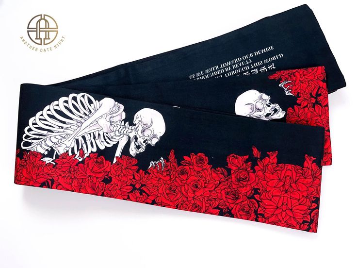 the image shows a long black scarf folded into three sections. each section is decorated with a different design. the first section features a white skeleton partially submerged in a patch of red roses. the middle section has a white skull and roses. the top section has a text print.