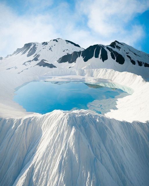 a serene aerial view of a frozen lake nestled within a snowcovered crater. the icy waters of the lake reflect the azure sky, creating a stunning contrast of colors. the surrounding snowcapped mountains, adorned with frost, add to the ethereal beauty of this winter wonderland. the stillness of the scene evokes a sense of tranquility and solitude, highlighting the aweinspiring power of nature.