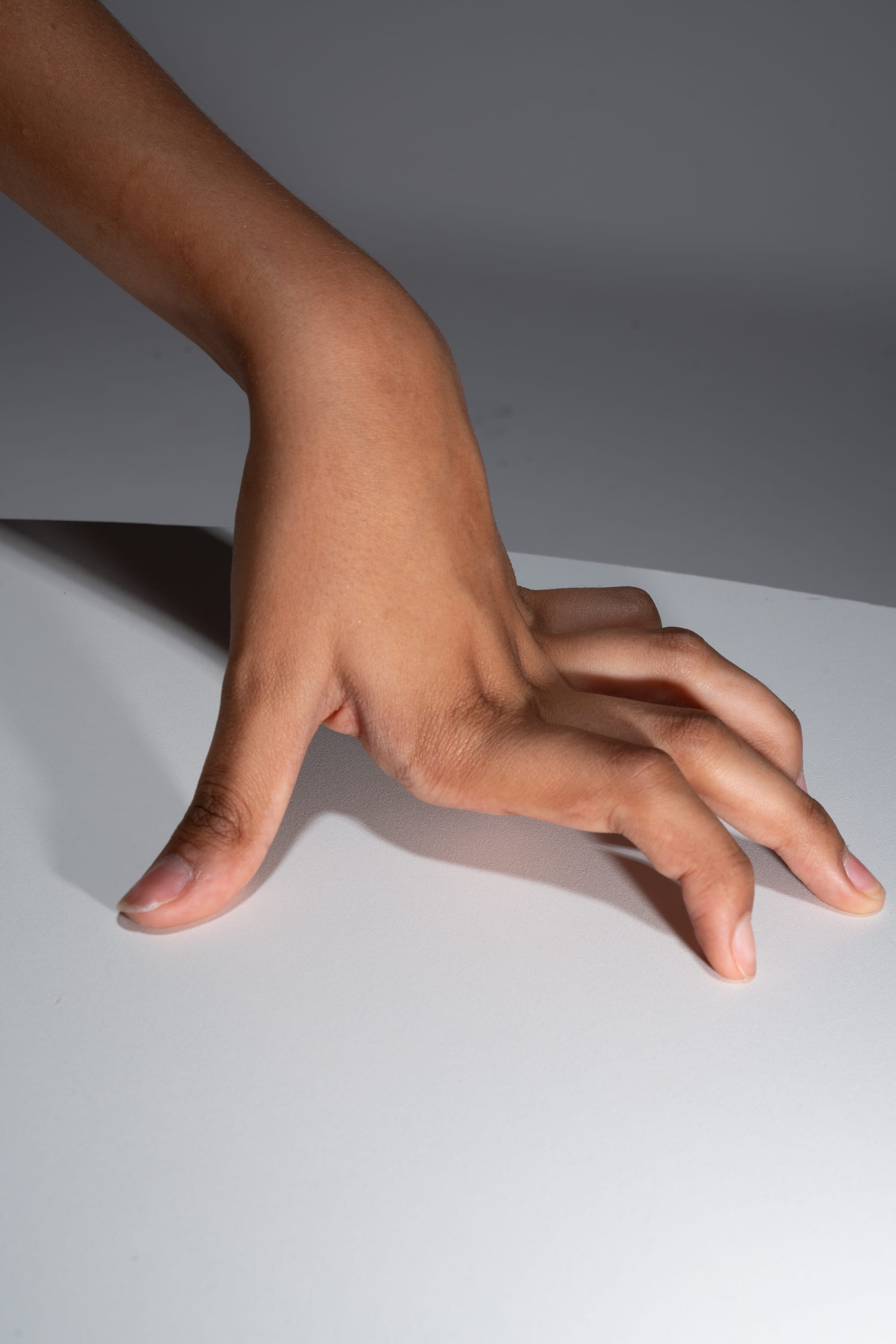 a hand is extended with fingers spread, resting on a white surface. the hand belongs to a person with darker skin tone.  the image is lit by studio lighting.