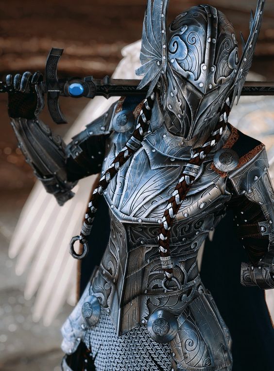a woman clad in ornate, silveretched armor stands in a powerful pose. she grips a large sword with a blue gem embedded in the hilt.  her helmet features winglike protrusions and her back is partially obscured by large, feathery wings. the low camera angle emphasizes her strength and creates a sense of grandeur. the setting appears to be weathered stone, hinting at a ruined environment.