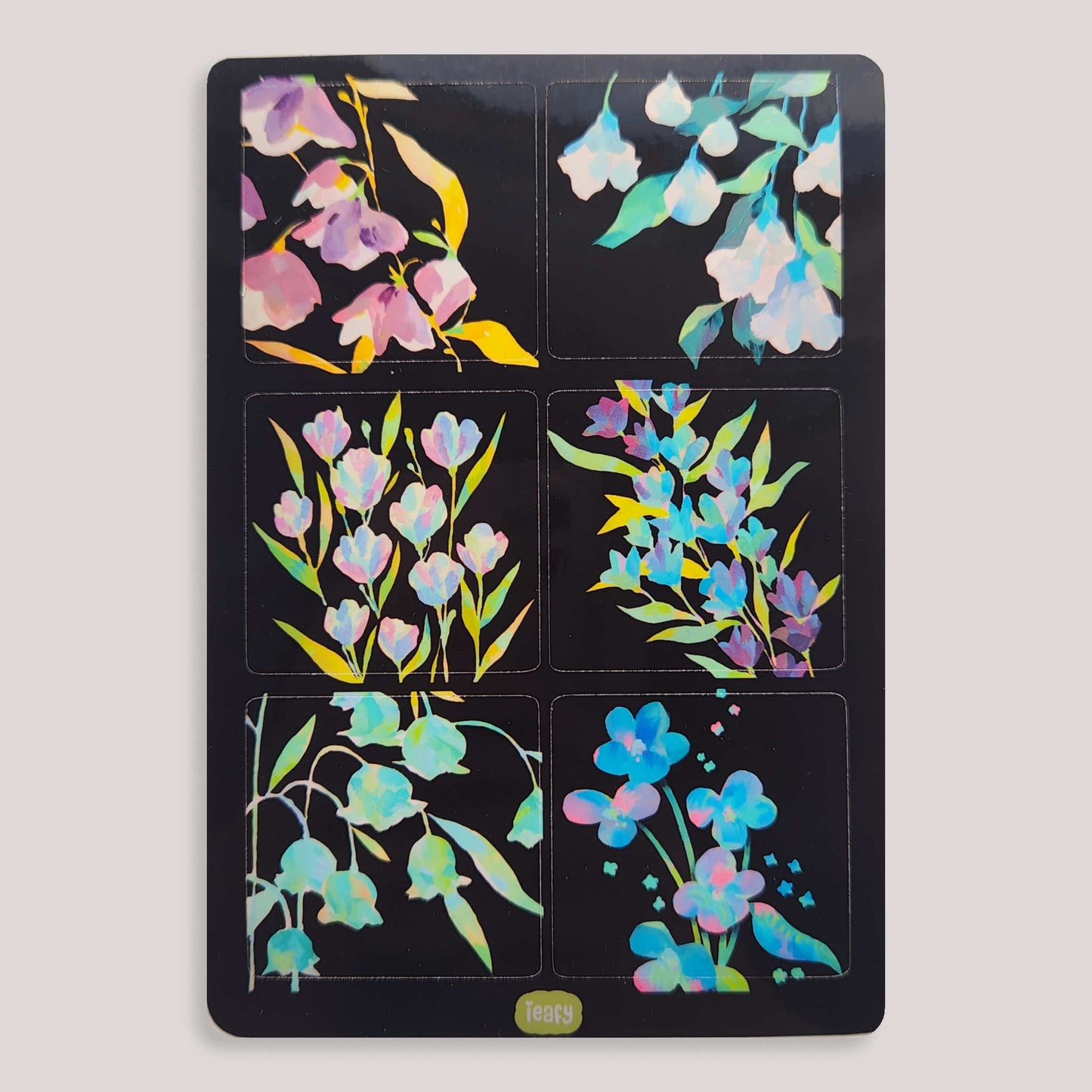 the image shows a sheet of six square stickers featuring different arrangements of pastelcolored flowers on a black background. the flowers appear to be rendered in a watercolor style and have an iridescent or holographic effect, giving them a shimmery appearance. the stickers are neatly arranged in a grid pattern on a black backing. a small, light green label with text is visible at the bottom.  the overall aesthetic is delicate and feminine.