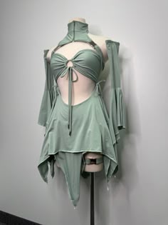 a closeup shot of a green highfashion outfit with a cutout detail, worn by a mannequin in a studio setting. the outfit features a halter top, a flowing skirt with an asymmetrical hem, and sleeves that fall to the elbows. the garment has a sophisticated, elegant feel and a modern design.