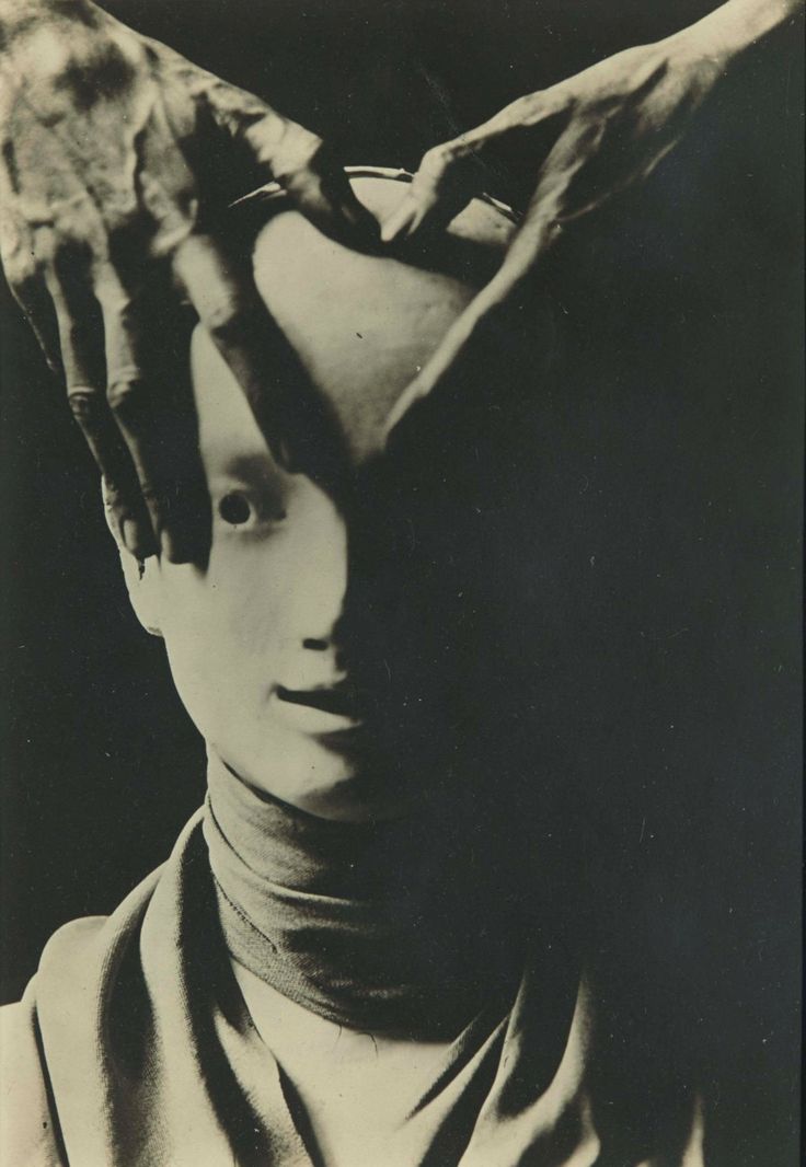 this is a vintage black and white photograph that looks like an artistic portrait. the photo appears to be of a woman's face, but her face is obscured by two hands. the hands are covering the woman's eyes, and the rest of her face is in shadow. the image is dark and mysterious, and it creates a sense of unease or even fear. the woman appears to be looking up at the hands, as if she is trying to see what is happening. the overall tone of the photo is one of mystery, intrigue, and fear.