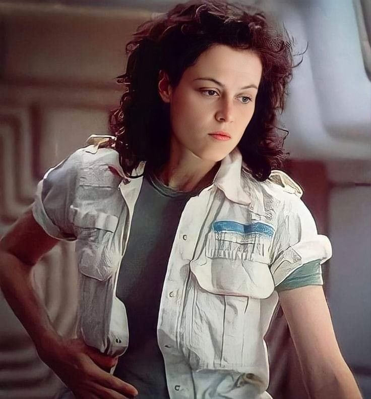 closeup portrait of a woman with dark curly hair. she is wearing a white shirt and jacket. her eyes are looking directly at the camera. the background is blurry. the image looks like a still from a movie. this is sigourney weaver as ellen ripley from the 1979 movie alien.