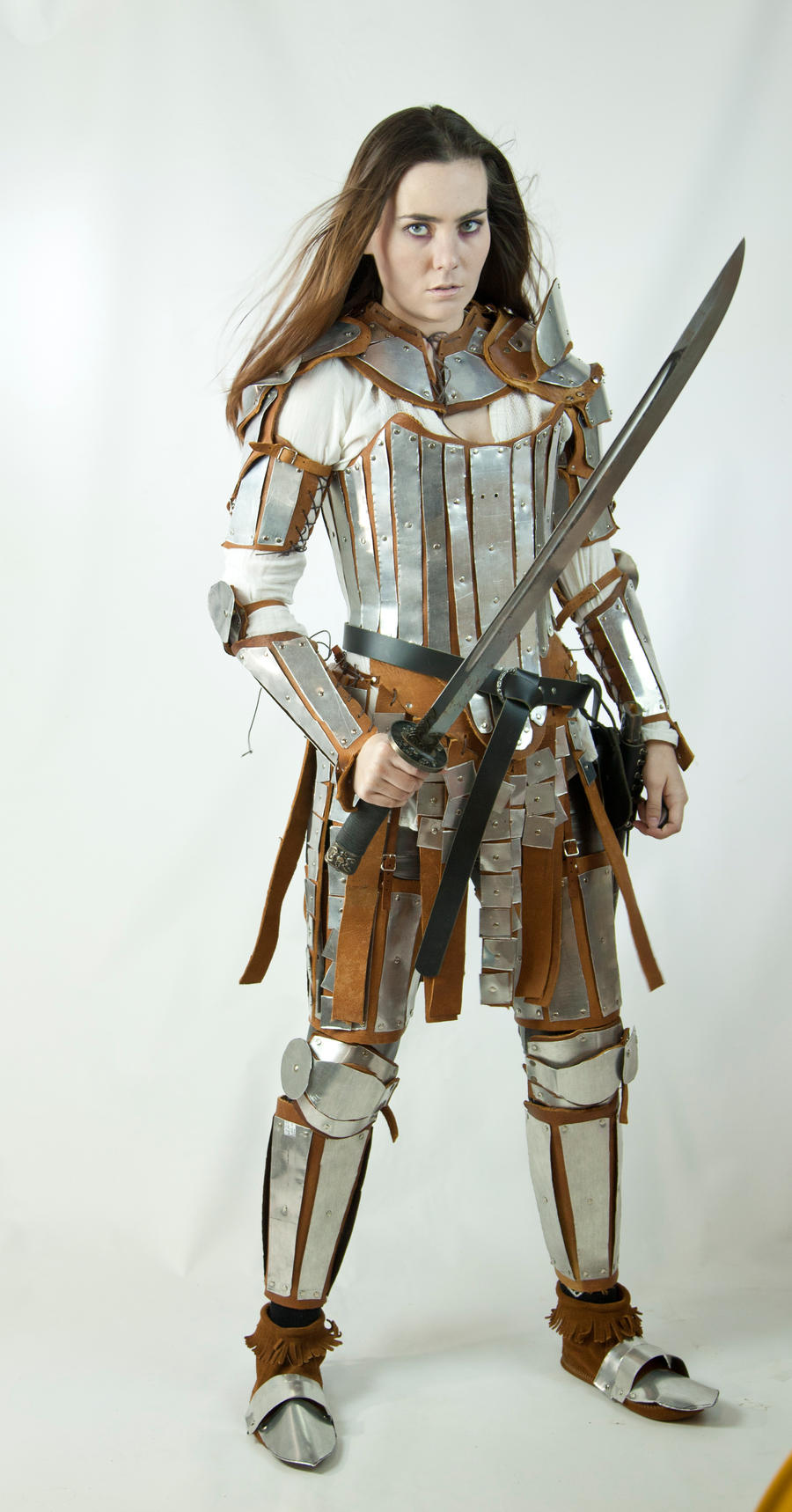 a fullbody shot of a female warrior, dressed in meticulously crafted fantasy armor. the armor consists of polished metal plates and brown leather accents, showing a blend of medieval and perhaps even japanese design influences.  she wears a corsetlike top underneath and the armor is highly detailed. she holds a long sword with a serious expression, presenting a powerful and commanding stance.  the background is plain white, focusing attention solely on the warrior and her attire. the costume suggests a character from a fantasy setting, potentially from a video game or film.