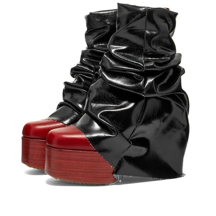 a pair of avantgarde platform boots with red toecaps and a reddishbrown wooden platform are displayed against a white background. the uppers of the boots are black and appear to be made of shiny, wrinkled leather, giving them a draped or scrunched appearance around the ankles and calves. the red toecaps contrast sharply with the black leather and brown platform, creating a bold and unconventional look.