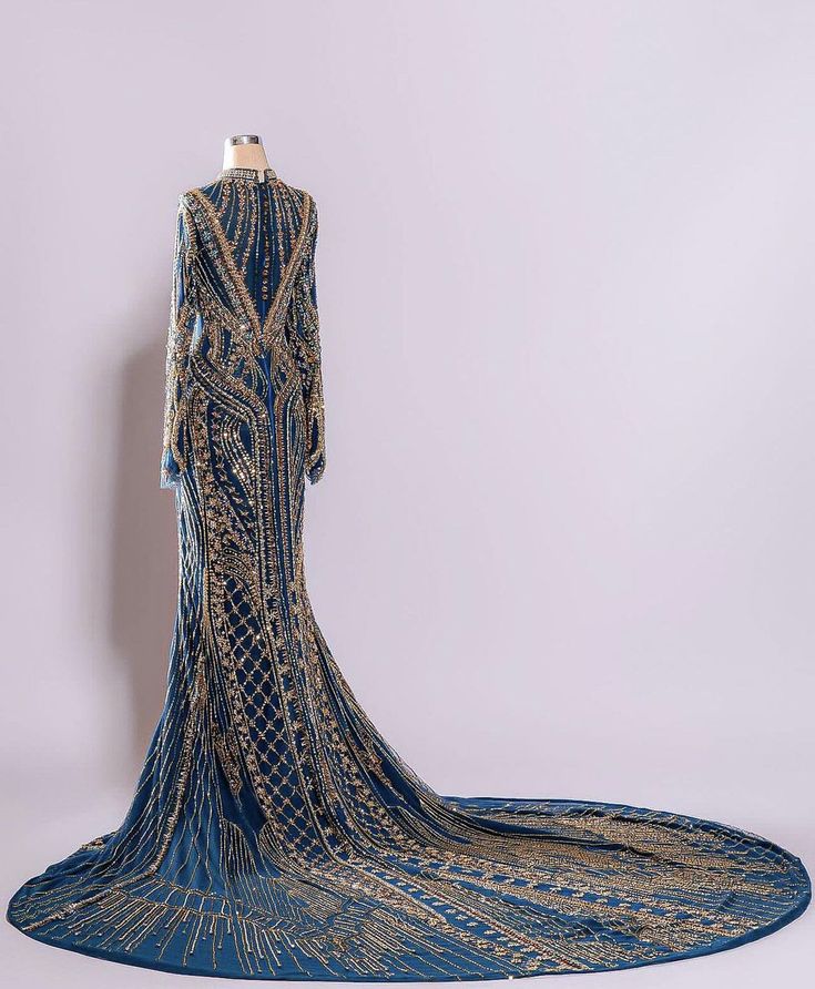 a long, blue gown with gold sequins is shown on a mannequin. the dress has a fitted bodice and a long, flowing train. the dress is adorned with intricate beading and sequins, which create a glamorous and elegant look. the dress is perfect for a special occasion, such as a wedding, prom, or gala.