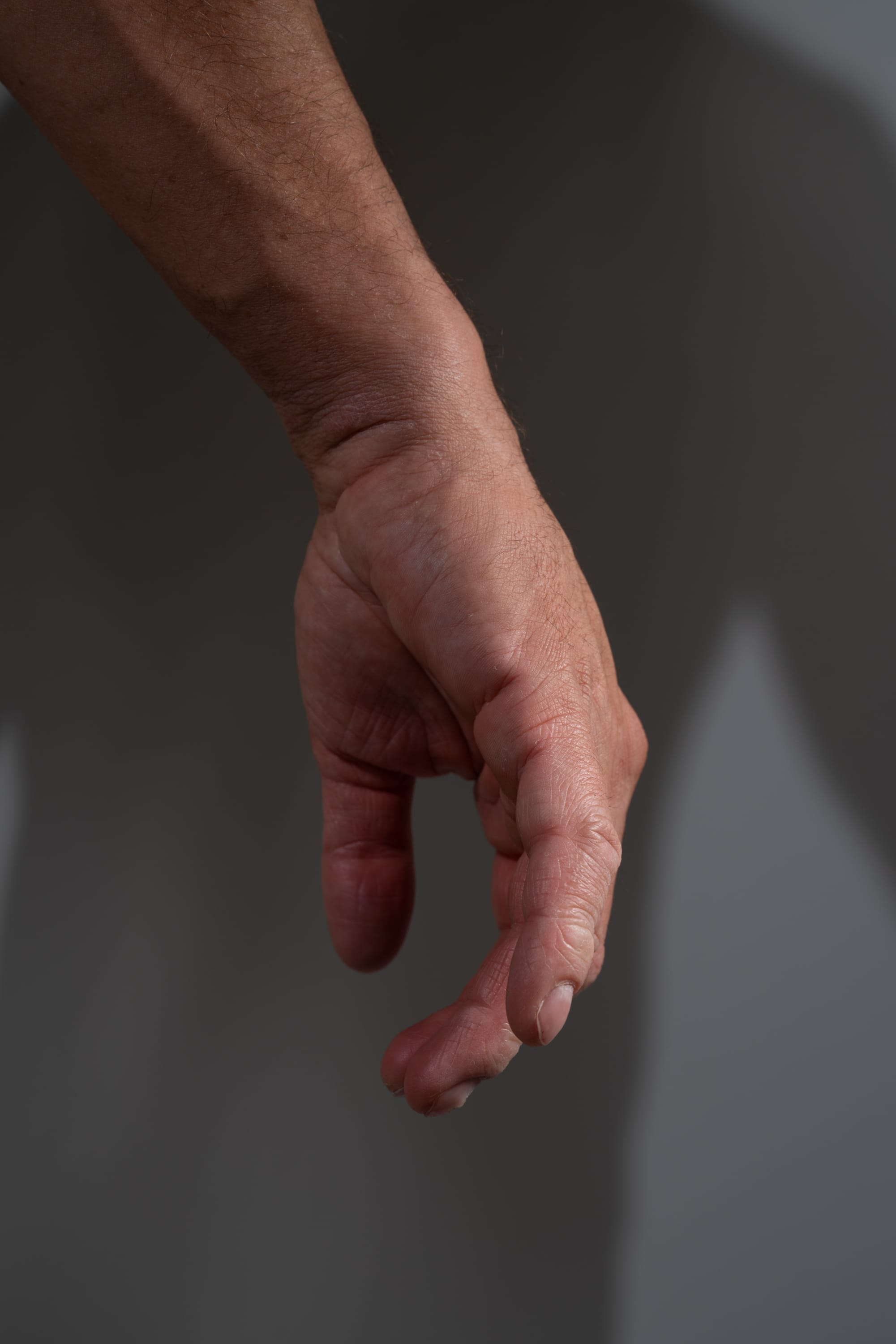 a closeup image of a man's hand and arm against a gray background. the hand is slightly cupped, as if reaching for something. the natural light creates a shadow on the background, adding depth and dimension to the image.
