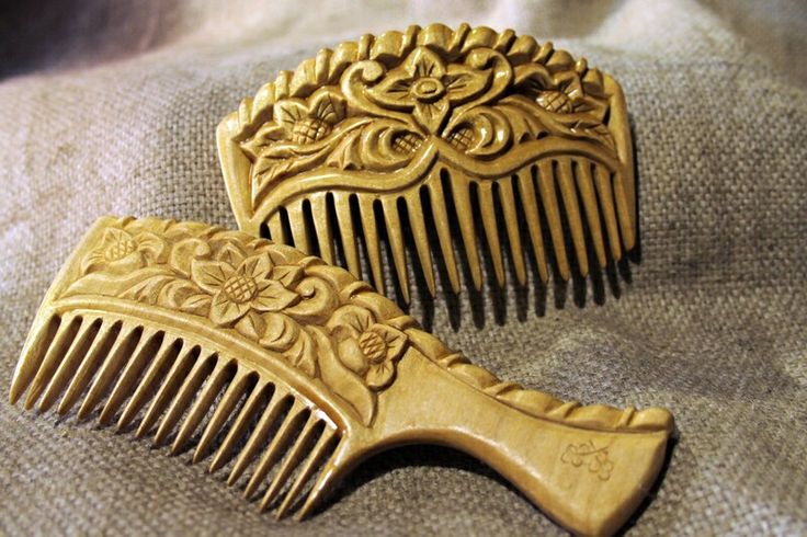 the image shows two intricately carved wooden combs resting on a textured fabric surface. the combs feature elaborate floral designs on their handles. one comb is rectangular, while the other has a handle. the warm tones of the wood and the detailed carvings highlight the craftsmanship involved in creating these decorative hair accessories.