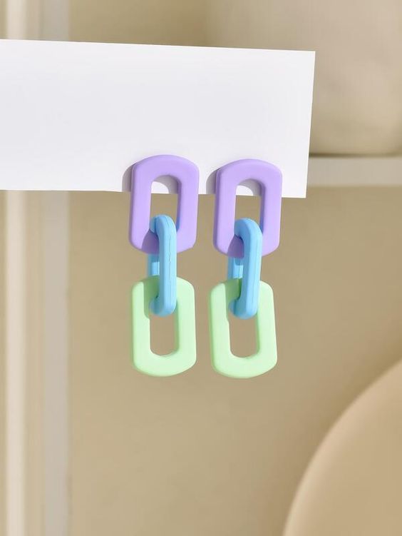 a closeup of a pair of pastelcolored chain earrings with a purple, light blue, and light green color scheme. the earrings are hanging from a white shelf.