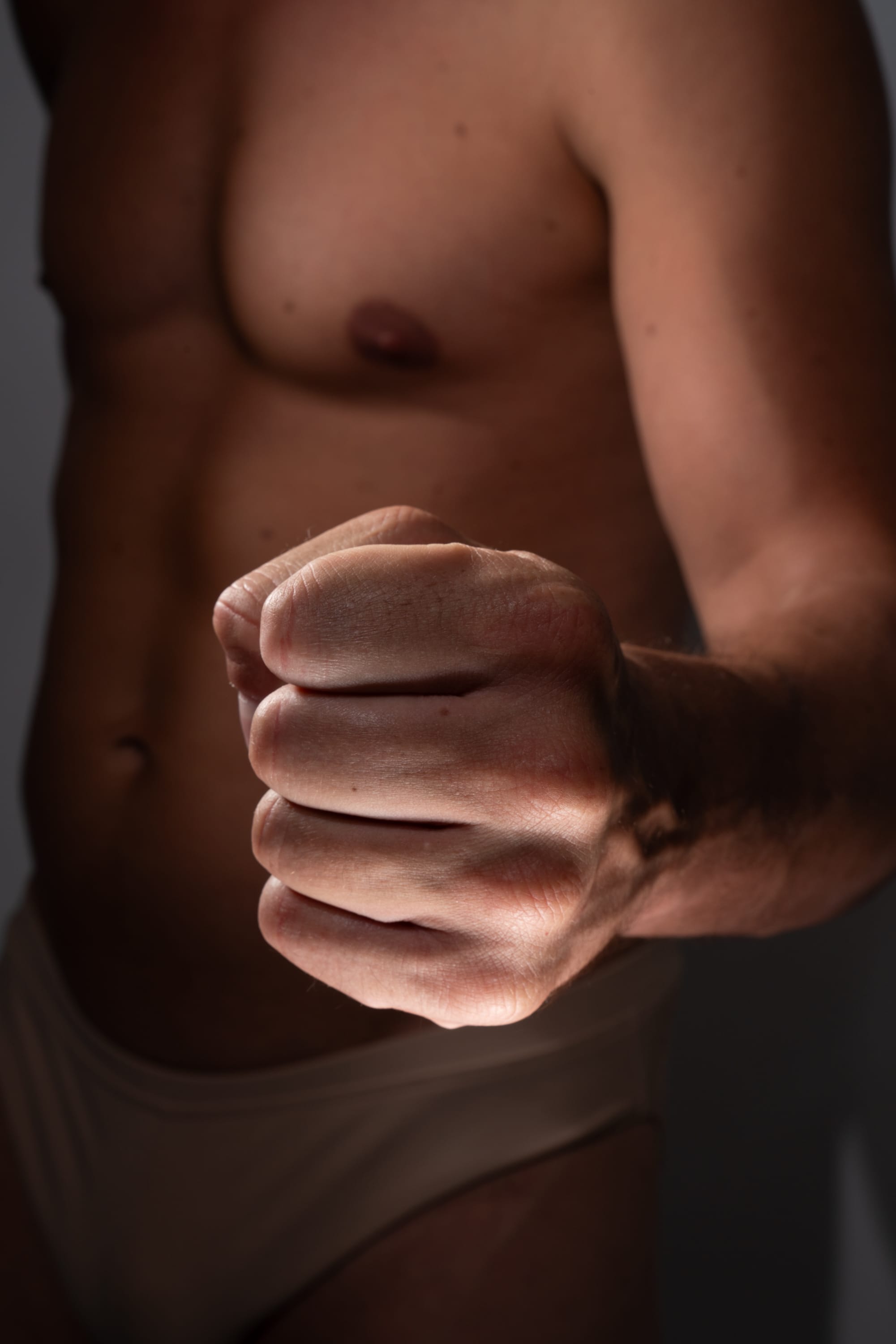 a closeup image of a muscular man's torso with his fist clenched in the foreground, conveying a