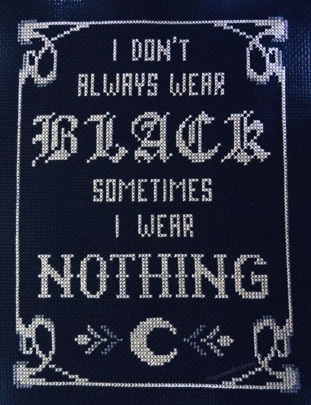 a closeup of a framed crossstitch artwork on dark blue fabric. the artwork is done in white thread. the image contains a gothicstyle border design at the top and bottom. inside the border, the text is stitched in a bold, slightly ornate font. the text reads: "i don't always wear black sometimes i wear nothing". below the text is a crescent moon symbol with decorative arrows on either side. the frame and stitches are visible.