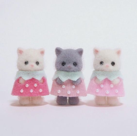the image shows three miniature calico critters or sylvanian families cat dolls. the dolls are arranged sidebyside, facing the viewer, and they are wearing pink dresses with pearl embellishments. the dolls have mint green collars. the dolls are on a plain white background.