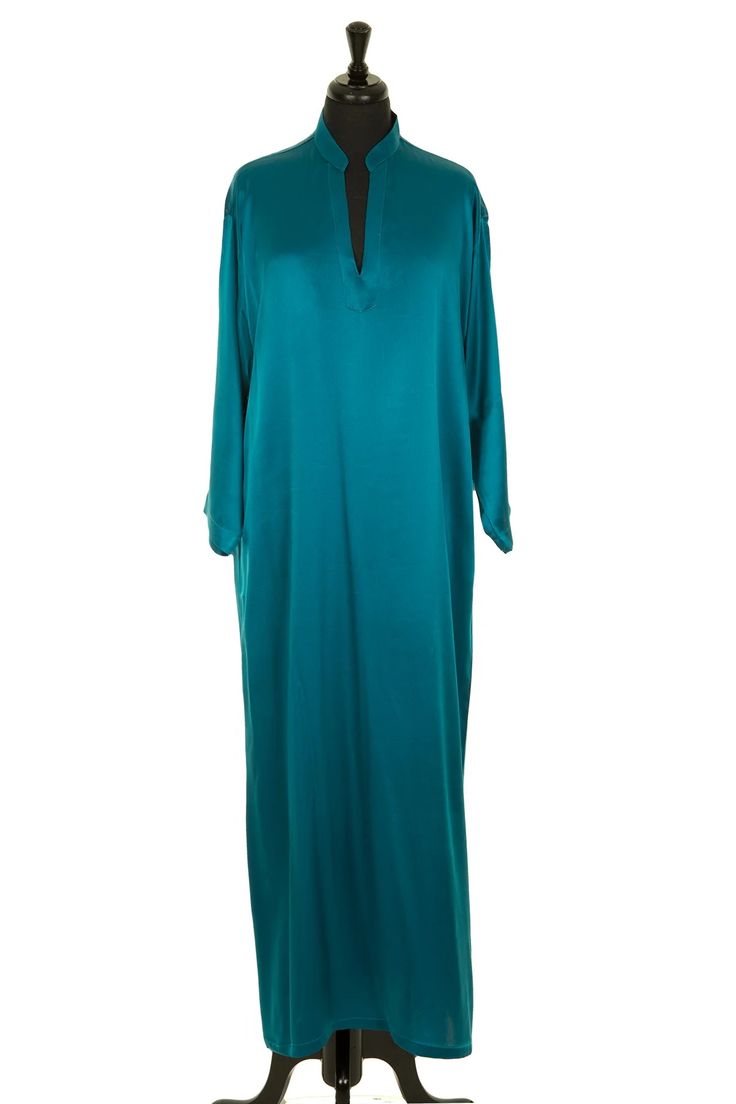 a teal blue longsleeved dress with a vneckline. the dress is made of silk and has a loosefitting, flowing silhouette. it is a kaftan style dress and is perfect for summer. the dress is displayed on a mannequin.