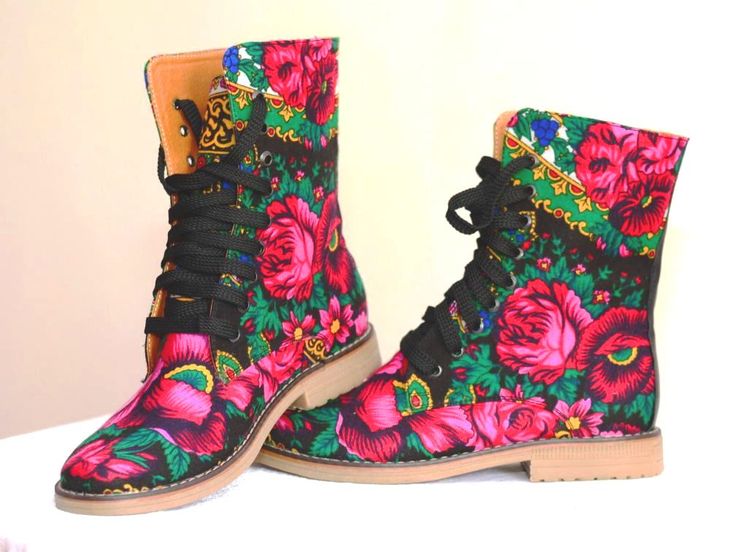 closeup shot showcases a pair of women's ankle boots adorned with a vibrant floral print. the boots are laceup style and feature a predominantly black background with bright pink, red, and green flowers. the floral pattern appears to be inspired by traditional folk art designs. the boots are set against a light beige background, enhancing their colorful appearance. one boot is slightly positioned in front of the other, providing a view of both from different angles. the image highlights the detailed and colorful nature of the boot's design.