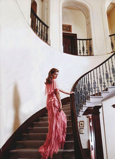 a woman in a flowing pink gown is descending a grand staircase in a luxurious mansion. the soft lighting and elegant pose create a sense of sophistication and glamour. the image exudes a timeless elegance, reminiscent of classic fashion photography.