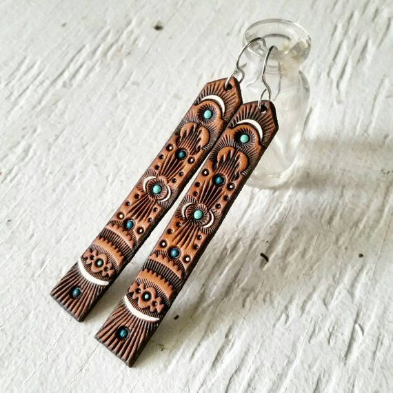 the image shows a pair of intricately carved wooden earrings with turquoise accents, displayed on a white surface next to a small, clear glass jar. the earrings feature a repeating decorative pattern. they have silver hooks for wearing.