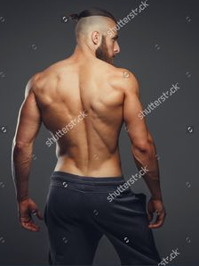 he image showcases a muscular man from the back, highlighting his welldefined back muscles and physique. he stands against a neutral gray background in a studio setting, illuminated by soft, artificial light. he is wearing dark grey sweatpants and his upper body is bare. the perspective offers a clear view of his back and the definition of his muscles, suggesting a focus on fitness and athleticism.