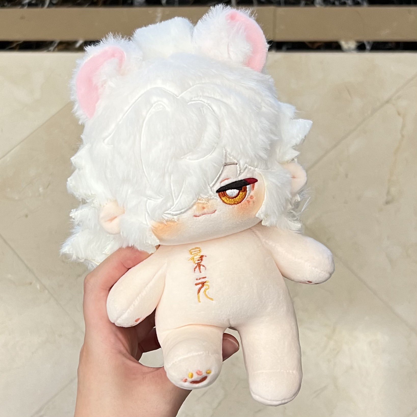 a plush toy in the form of a whitehaired humanlike figure with pink ears. it has a soft, fluffy texture and a cute, animeinspired face. the toy is sitting in a hand, showcasing its cuddly nature.