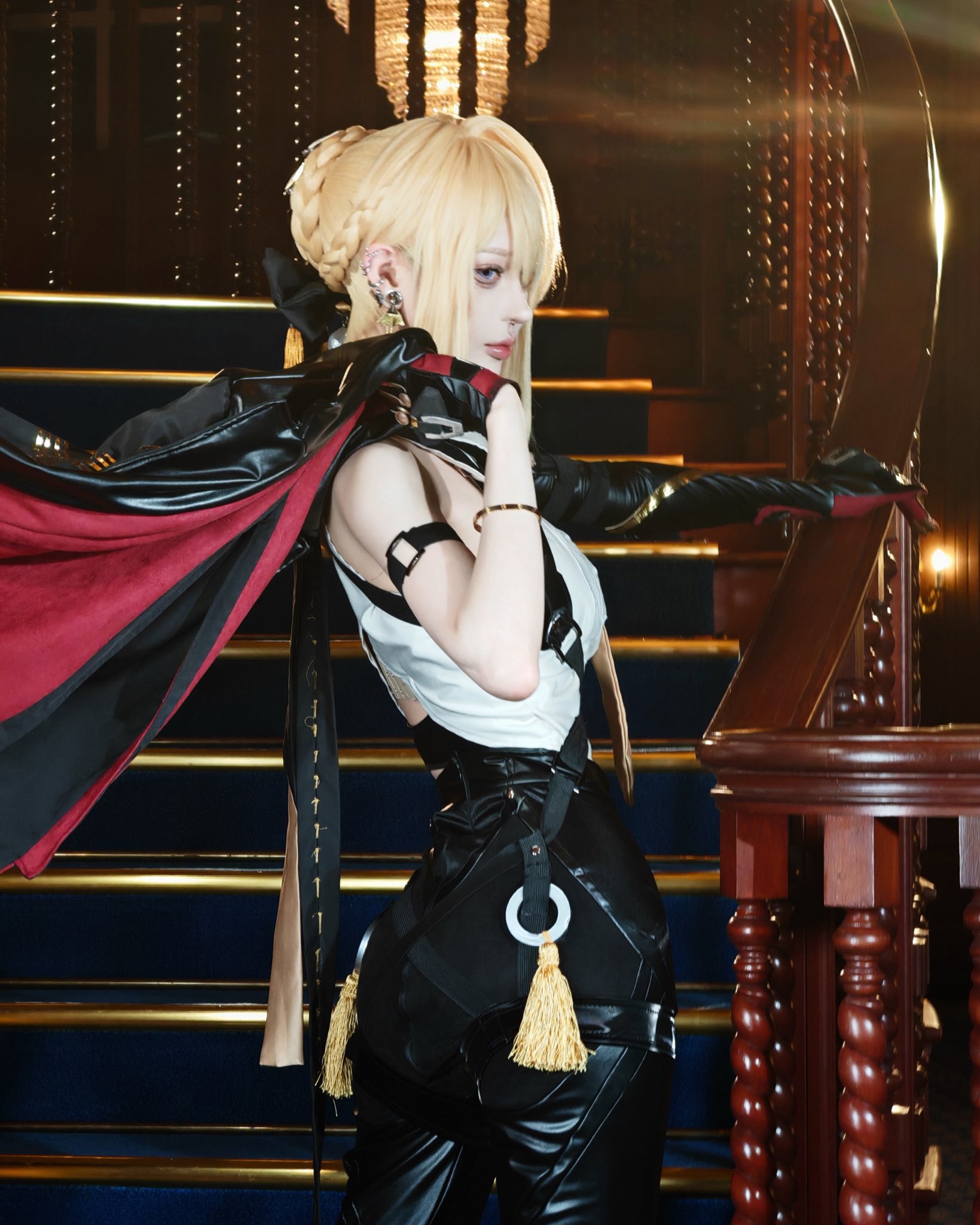a captivating cosplay photograph features a woman meticulously portraying a character, possibly from an anime or video game.  her blonde hair is elegantly braided, complementing her dark, leatherbased outfit adorned with gold accents. she strikes a dramatic pose on a grand staircase, the dark setting and lighting enhancing the overall mood of elegance and mystery.  the costume's detail is impressive, showcasing meticulous craftsmanship and attention to character accuracy. the image displays highquality photography, focusing on both the character and the environment.